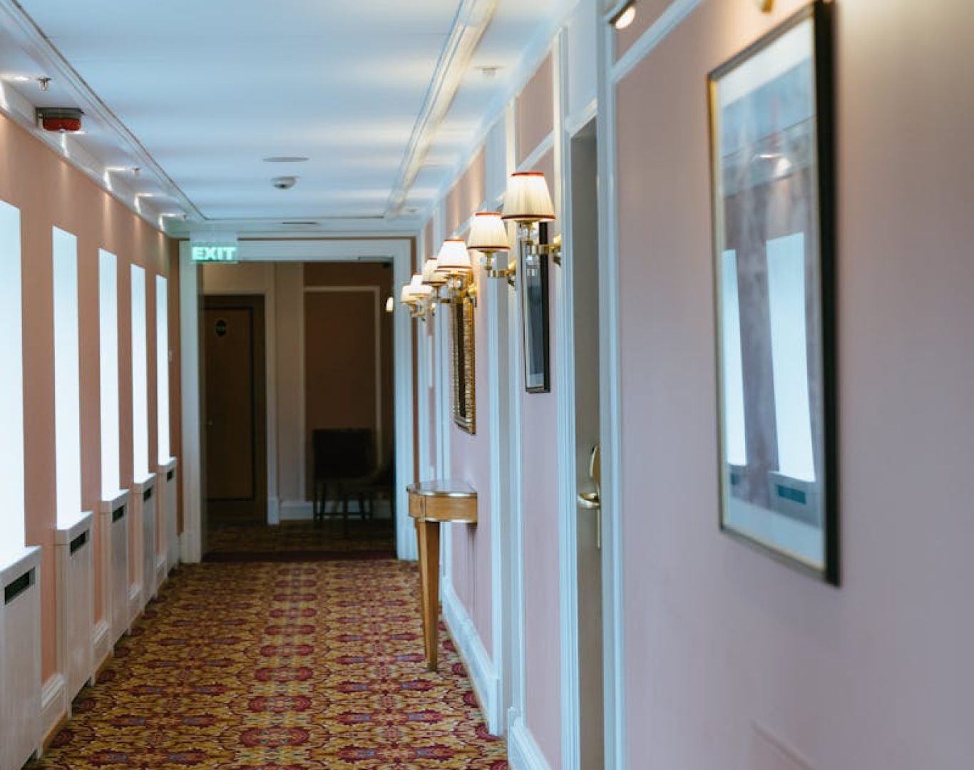 Well-lit hotel corridor with ornate carpet and framed art, offering a cozy atmosphere.